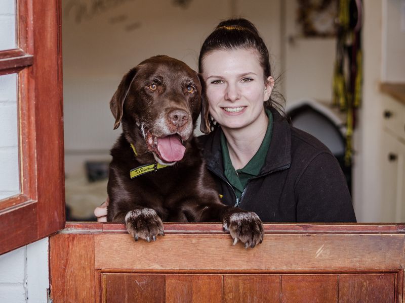 Pip the chocolate Labrador and Canine Carer Elizabeth posing in the doorway of Oakfield Oldies
